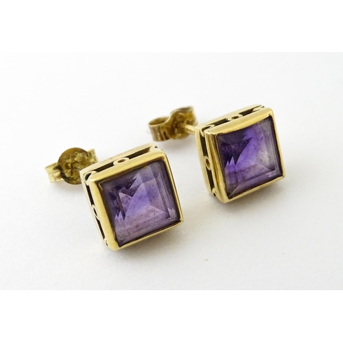 673 - A pair of yellow metal stud earrings of squared form set with amethyst. Approx. 1/4