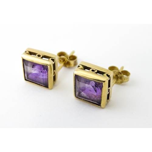 673 - A pair of yellow metal stud earrings of squared form set with amethyst. Approx. 1/4