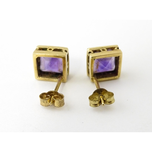 673 - A pair of yellow metal stud earrings of squared form set with amethyst. Approx. 1/4