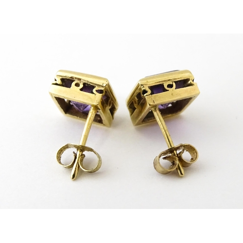 673 - A pair of yellow metal stud earrings of squared form set with amethyst. Approx. 1/4