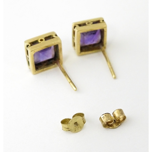 673 - A pair of yellow metal stud earrings of squared form set with amethyst. Approx. 1/4