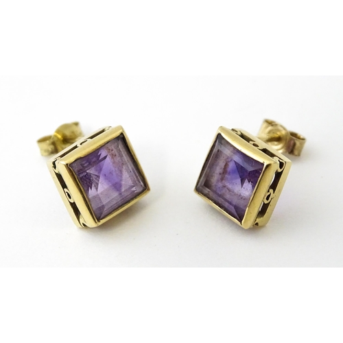 673 - A pair of yellow metal stud earrings of squared form set with amethyst. Approx. 1/4