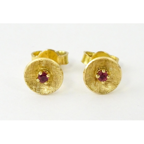 696 - A pair of yellow metal stud earrings set with red stones to centre. Approx. 1/4