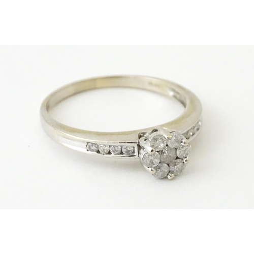 710 - An 18ct white gold ring having 7 diamonds in a daisy setting flanked by four diamonds to shoulders. ... 