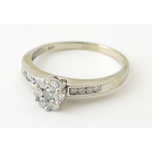 710 - An 18ct white gold ring having 7 diamonds in a daisy setting flanked by four diamonds to shoulders. ... 