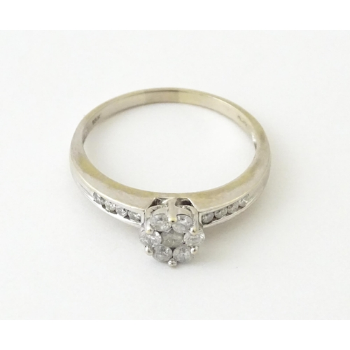 710 - An 18ct white gold ring having 7 diamonds in a daisy setting flanked by four diamonds to shoulders. ... 