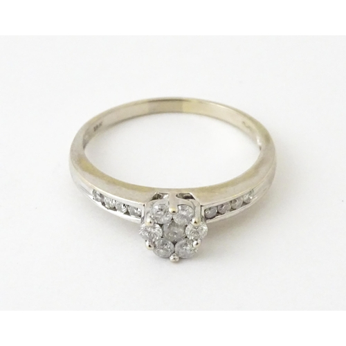 710 - An 18ct white gold ring having 7 diamonds in a daisy setting flanked by four diamonds to shoulders. ... 