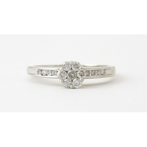 710 - An 18ct white gold ring having 7 diamonds in a daisy setting flanked by four diamonds to shoulders. ... 