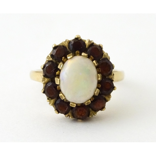 714 - A 9ct gold ring set with central opal bordered by garnets. Ring size approx. K 1/2