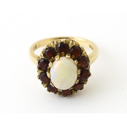 714 - A 9ct gold ring set with central opal bordered by garnets. Ring size approx. K 1/2