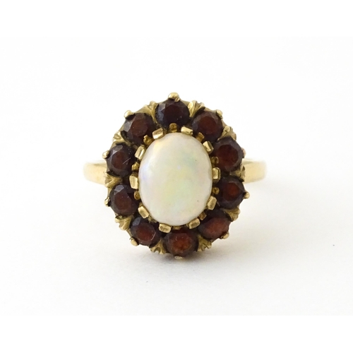 714 - A 9ct gold ring set with central opal bordered by garnets. Ring size approx. K 1/2