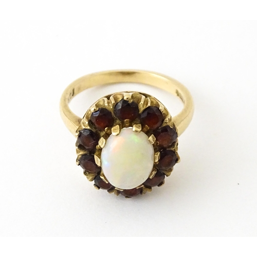 714 - A 9ct gold ring set with central opal bordered by garnets. Ring size approx. K 1/2