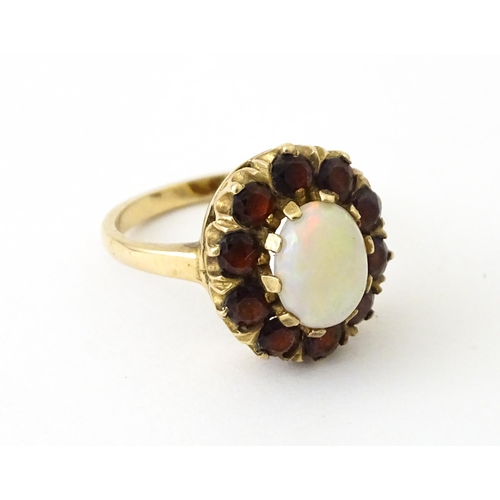 714 - A 9ct gold ring set with central opal bordered by garnets. Ring size approx. K 1/2