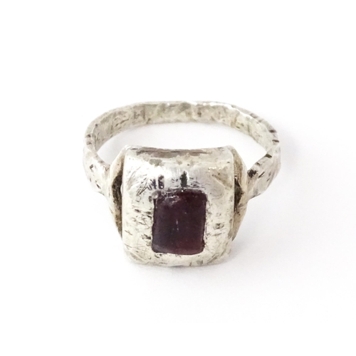 720 - A white metal ring with hammered and engraved detail set with central red coloured stone. Ring size ... 