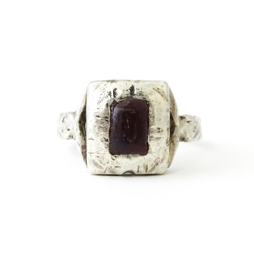 720 - A white metal ring with hammered and engraved detail set with central red coloured stone. Ring size ... 