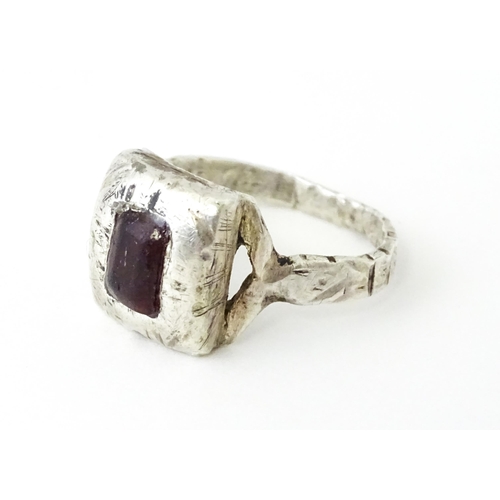 720 - A white metal ring with hammered and engraved detail set with central red coloured stone. Ring size ... 