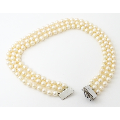 769 - A three strand pearl choker necklace with 14ct white gold clasp set with diamonds, sapphires, and pe... 