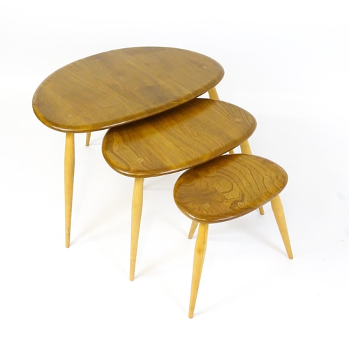 1638 - An Ercol nest of three elm pebble tables raised on turned tapering legs. 26