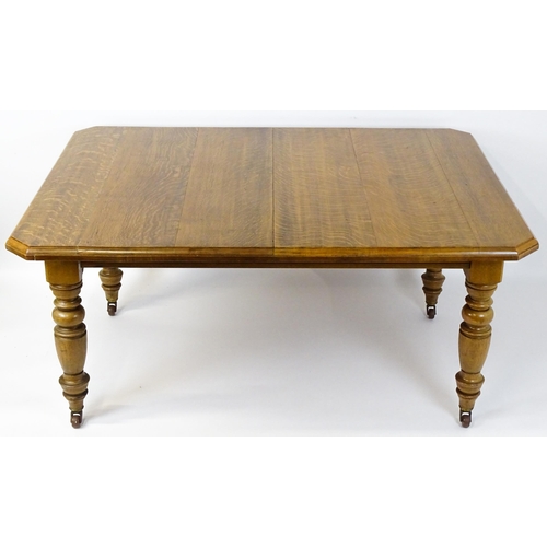 1442 - A late 19thC / early 20thC oak dining table with canted corners raised on turned tapering legs termi... 