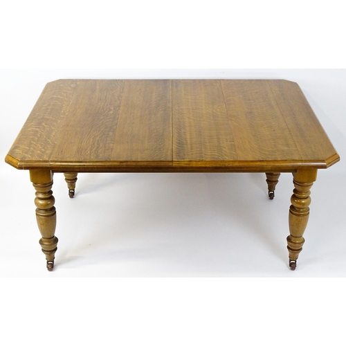 1442 - A late 19thC / early 20thC oak dining table with canted corners raised on turned tapering legs termi... 