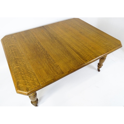 1442 - A late 19thC / early 20thC oak dining table with canted corners raised on turned tapering legs termi... 