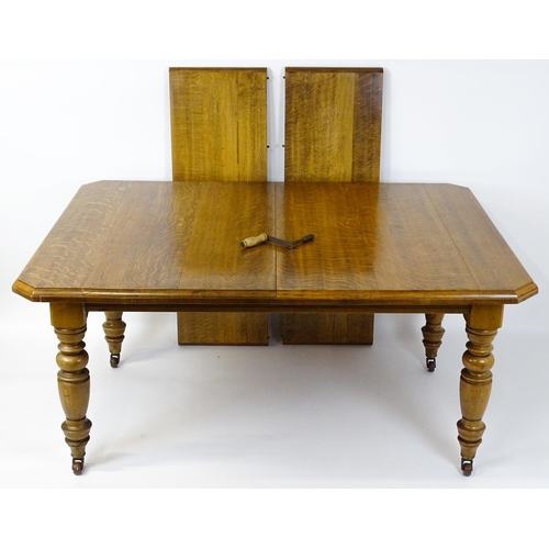 1442 - A late 19thC / early 20thC oak dining table with canted corners raised on turned tapering legs termi... 