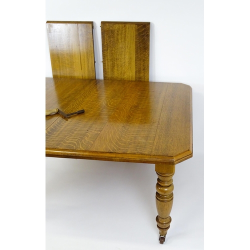 1442 - A late 19thC / early 20thC oak dining table with canted corners raised on turned tapering legs termi... 