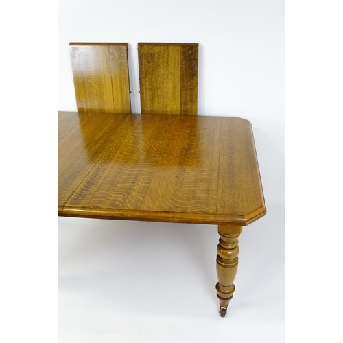 1442 - A late 19thC / early 20thC oak dining table with canted corners raised on turned tapering legs termi... 