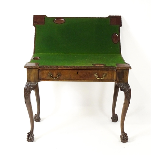 1449 - An Irish Chippendale mahogany card table with a carved inverted breakfront top, opening to show a ba... 