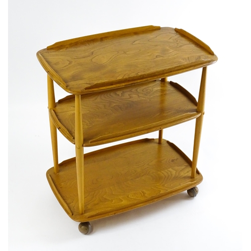 1630 - Vintage / Retro : An elm Ercol three tier trolley with shaped upstands, and turned uprights raised o... 