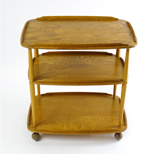 1630 - Vintage / Retro : An elm Ercol three tier trolley with shaped upstands, and turned uprights raised o... 