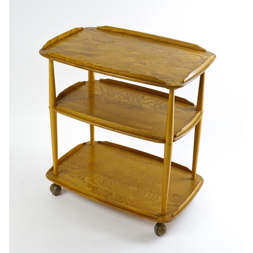 1630 - Vintage / Retro : An elm Ercol three tier trolley with shaped upstands, and turned uprights raised o... 