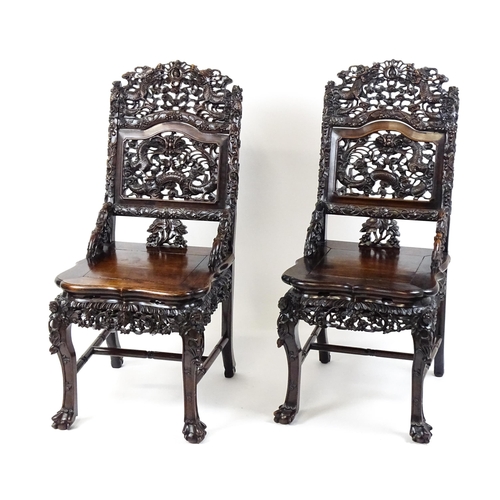 1452 - A pair of late 19thC / early 20thC Chinese hardwood side chairs with intricately carved frames depic... 