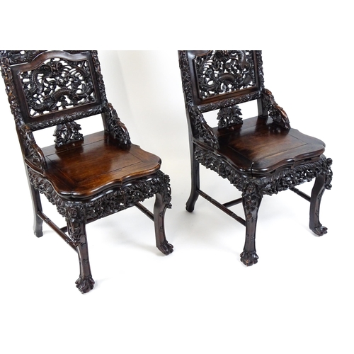 1452 - A pair of late 19thC / early 20thC Chinese hardwood side chairs with intricately carved frames depic... 