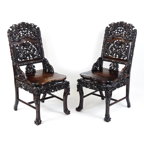 1452 - A pair of late 19thC / early 20thC Chinese hardwood side chairs with intricately carved frames depic... 