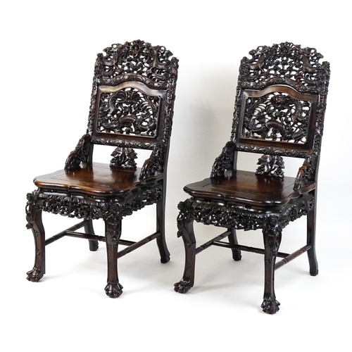 1452 - A pair of late 19thC / early 20thC Chinese hardwood side chairs with intricately carved frames depic... 