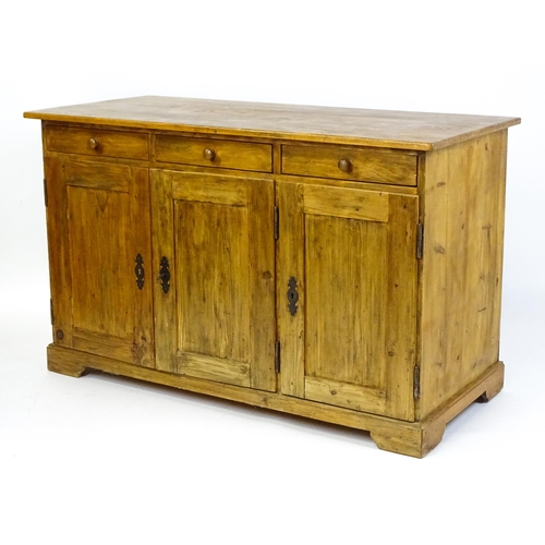 1494 - A 20thC pine sideboard with three short drawers above three panelled cupboard doors raised on bracke... 