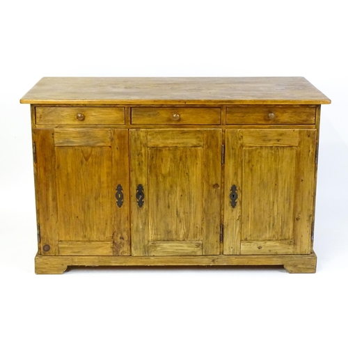 1494 - A 20thC pine sideboard with three short drawers above three panelled cupboard doors raised on bracke... 