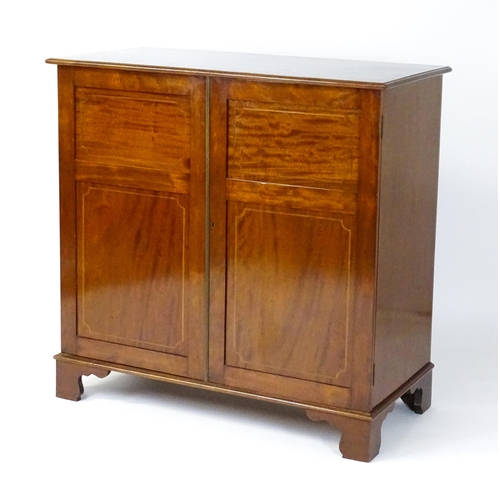 1498 - A mid 20thC mahogany cabinet with a moulded top above two panelled doors raised on ogee bracket feet... 