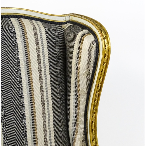 1557 - A Louis XVI style wingback armchair with a white and gold painted frame, striped upholstery and rais... 