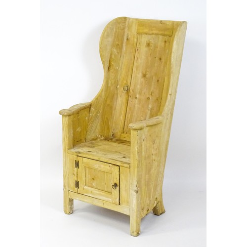 1571 - A pine lambing chair with a wingback above a planked seat and a cupboard to the base with H-bracket ... 