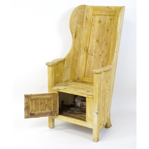 1571 - A pine lambing chair with a wingback above a planked seat and a cupboard to the base with H-bracket ... 