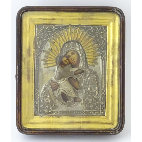 1054 - A 19thC Russian oil on panel icon depicting Madonna and Child with an embossed white metal surround ... 