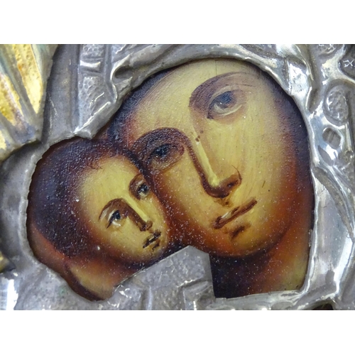 1054 - A 19thC Russian oil on panel icon depicting Madonna and Child with an embossed white metal surround ... 