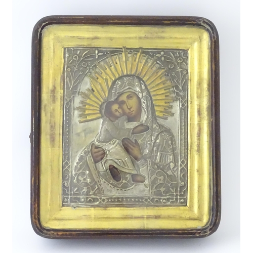 1054 - A 19thC Russian oil on panel icon depicting Madonna and Child with an embossed white metal surround ... 