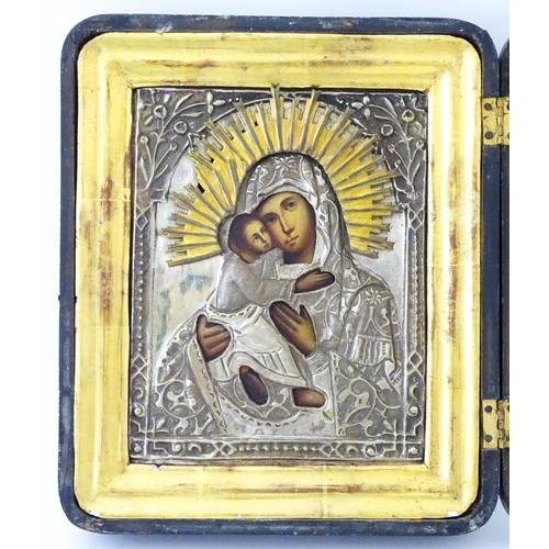 1054 - A 19thC Russian oil on panel icon depicting Madonna and Child with an embossed white metal surround ... 