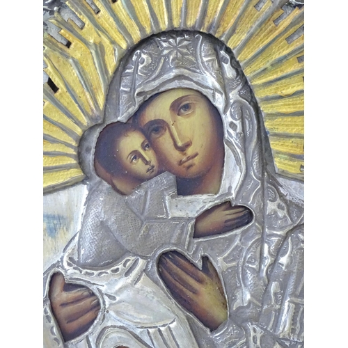 1054 - A 19thC Russian oil on panel icon depicting Madonna and Child with an embossed white metal surround ... 