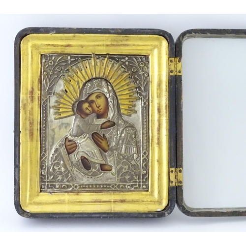 1054 - A 19thC Russian oil on panel icon depicting Madonna and Child with an embossed white metal surround ... 