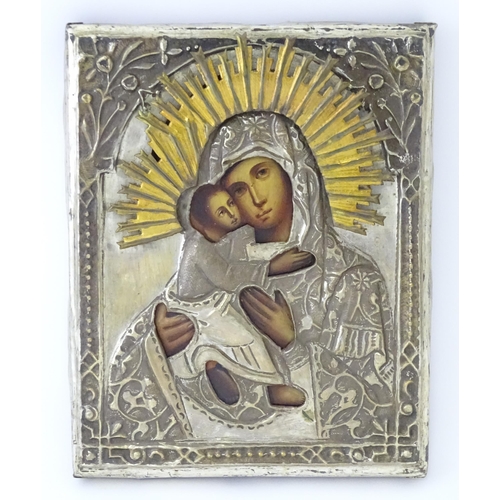 1054 - A 19thC Russian oil on panel icon depicting Madonna and Child with an embossed white metal surround ... 