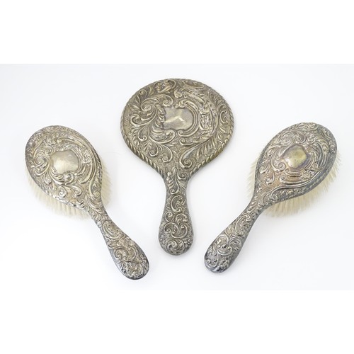 516 - A set of three silver dressing table items with embossed decoration comprising hand mirror and two b... 